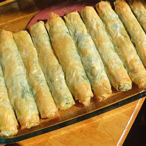 Golden, crispy spinach and feta borek rolls made with phyllo dough, served on a rustic platter with a side of yogurt dip.