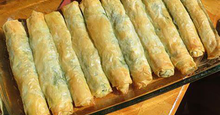 Golden, crispy spinach and feta borek rolls made with phyllo dough, served on a rustic platter with a side of yogurt dip.