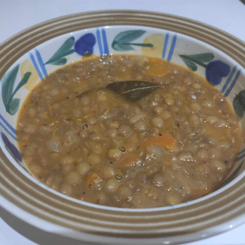 A bowl of traditional Greek lentil soup with brown lentils, carrots, and a drizzle of olive oil, served with crusty bread.
