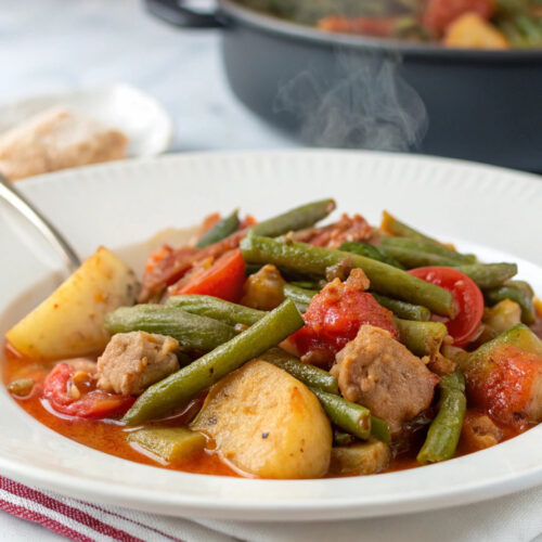 A bowl of traditional Greek Fasolakia Lathera with green beans in rich tomato sauce, garnished with fresh herbs