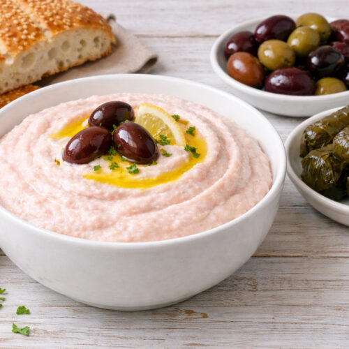 Traditional Greek taramosalata served in a white bowl with lagana bread, Kalamata olives, and dolmadakia on the side, garnished with olive oil and lemon.