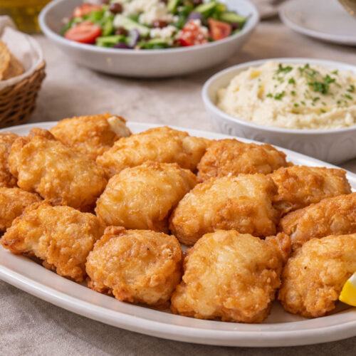 Greek fried cod in traditional batter served with skordalia, salad, bread and white wine on a dining table